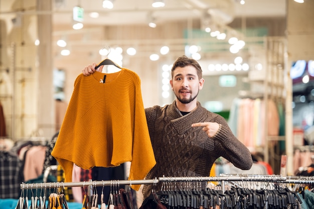 A teenager helping his girlfriend to find the right sweater in a clothing store.