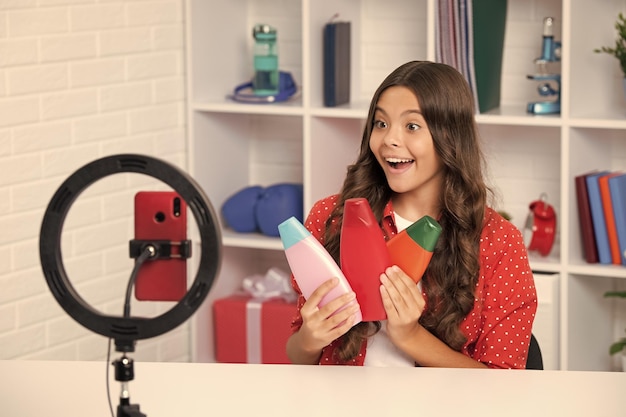 Подросток держит кондиционер для волос или бутылку с шампунем, записывая онлайн-медиа-видео Девушка-подросток в потоковом режиме