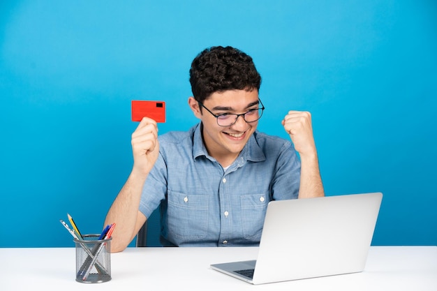 Teenager holding credit card in front of laptop isolated on blue background