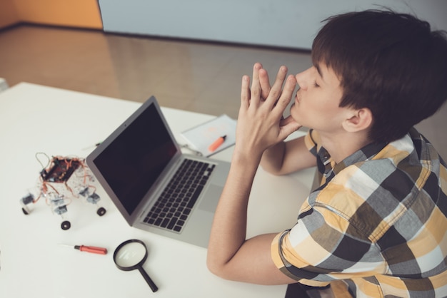 A teenager is sitting at a table in front of a laptop 