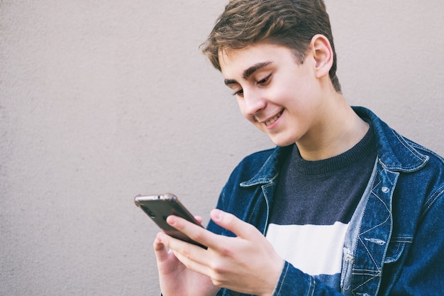 Teenager is using the phone and smiling - Happy teenager holding the phone in his hand