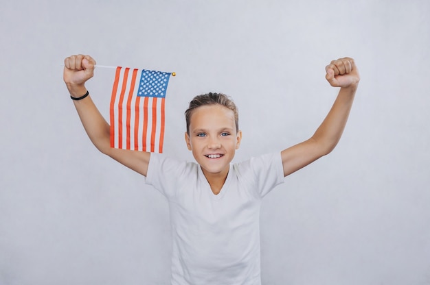 Foto adolescente su uno sfondo chiaro che tiene una bandiera americana nelle sue mani.