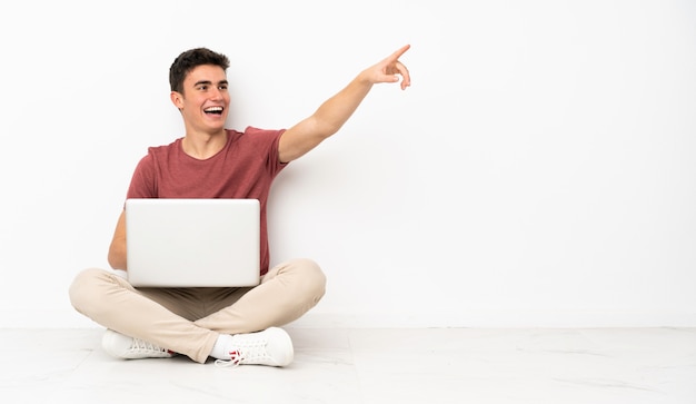 Teenager man sitting on the flor with his laptop pointing away