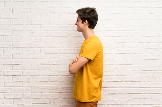 Teenager man over white brick wall in lateral position