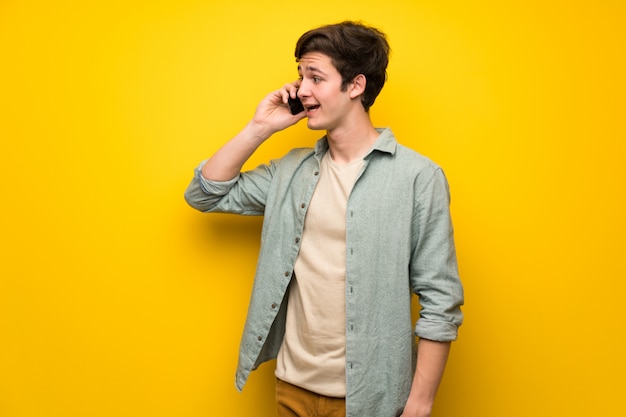 Photo teenager man over yellow wall keeping a conversation with the mobile phone