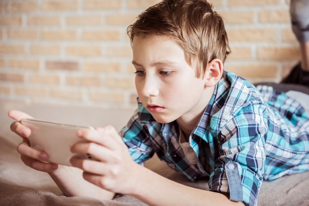 Teenager messaging to friends chat on mobile lying on couch in living room at home