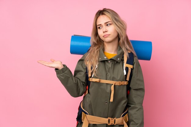 Teenager mountaineer girl with a big backpack on pink wall holding blank space with doubts