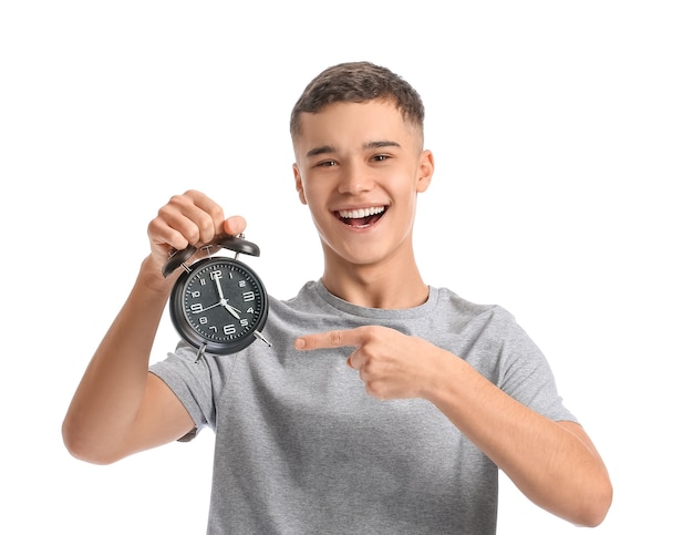 Teenager in pajamas and with alarm clock on white background