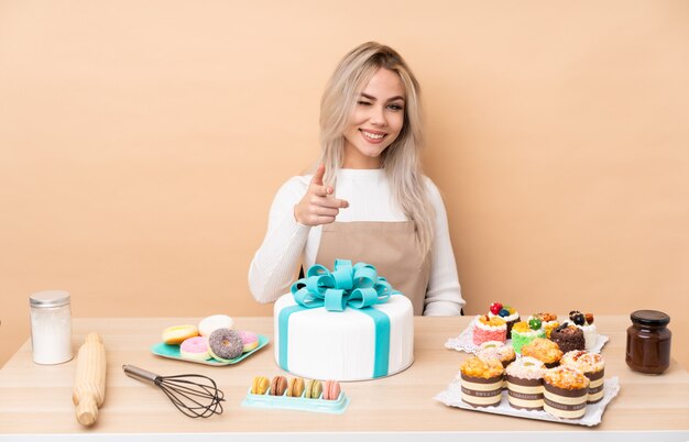 Pasticcere adolescente con una grande torta in un tavolo punta il dito su di te