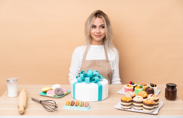 Teenager pastry chef with a big cake in a table standing and looking to the side