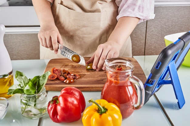 Foto l'adolescente prepara gli spaghetti alla bolognese da un libro di testo online e guarda la ricetta digitale sul tablet touchscreen mentre prepara un pasto sano nella cucina di casa