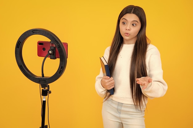 Teenager recording online media video Teen girl streaming online and sharing social media content by mobile phone app network isolated on yellow studio background