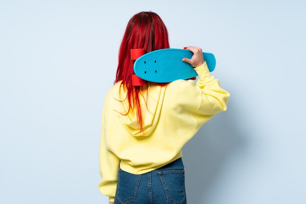 Teenager red hair girl on blue wall with a skate in back position