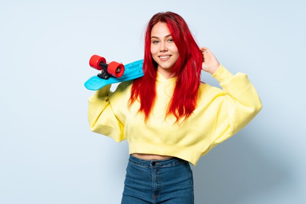 Teenager red hair woman isolated on blue wall with a skate
