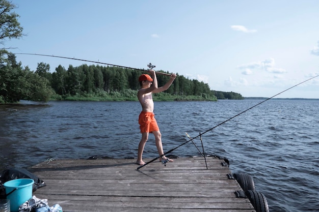 A teenager in red shorts and a red baseball cap fishes in the river Summer vacation