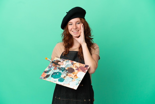 Teenager redhead artist holding a palette isolated on green background shouting with mouth wide open