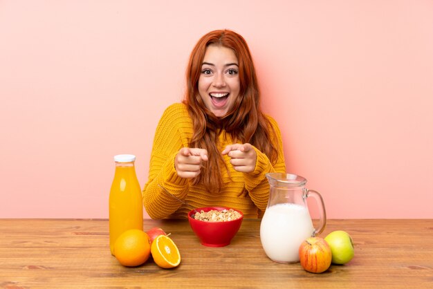 Teenager redhead girl having breakfast in a table points finger at you