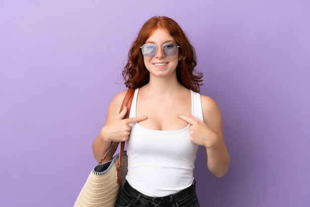 Teenager redhead girl holding a beach bag isolated on purple background with surprise facial expression