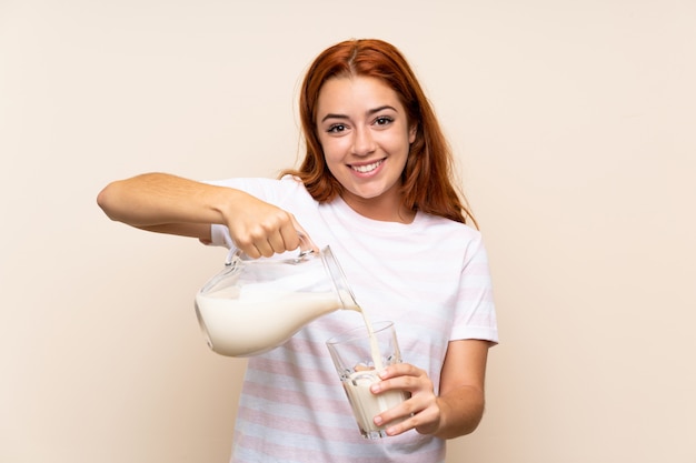 Teenager redhead girl holding a glass of milk over isolated wall