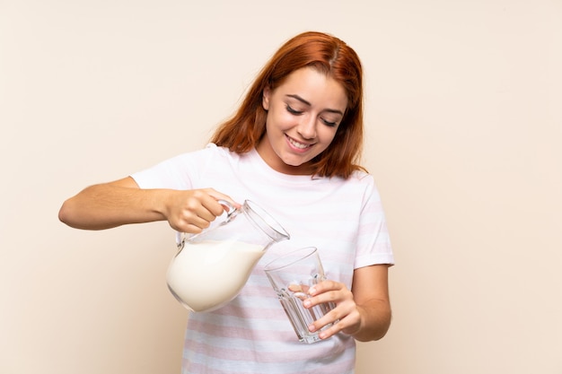 Teenager redhead girl holding a glass of milk over isolated