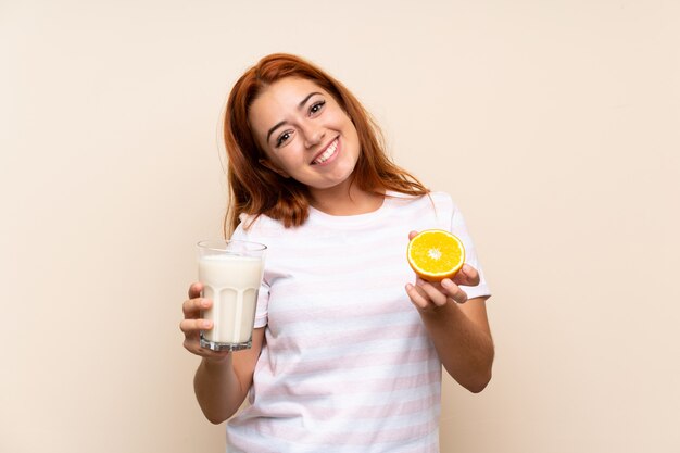 Рыжая девушка-подросток держит стакан молока и апельсин