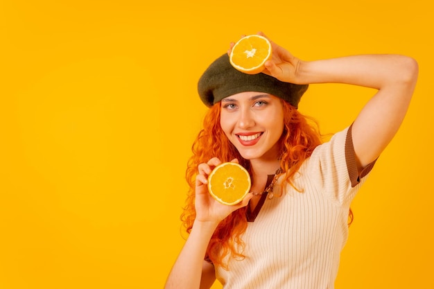 Teenager redhead girl holding an orange on isolated yellow background