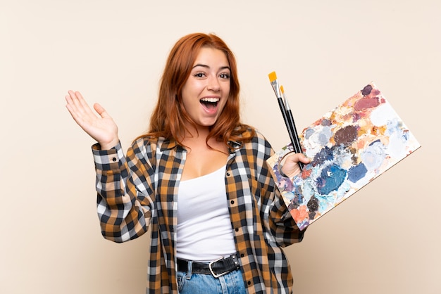 Teenager redhead girl holding a palette applauding