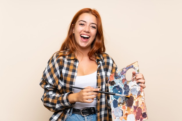 Teenager redhead girl holding a palette over isolated wall