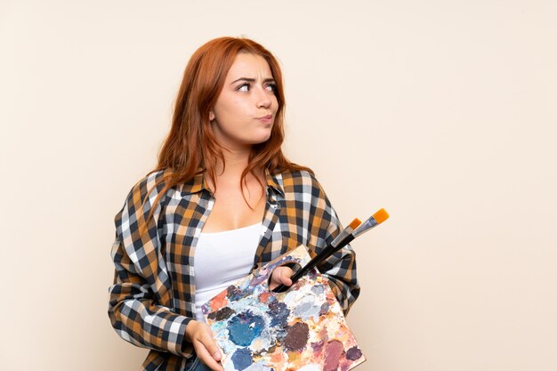 Ragazza della testarossa dell'adolescente che tiene una tavolozza che sta e che guarda al lato