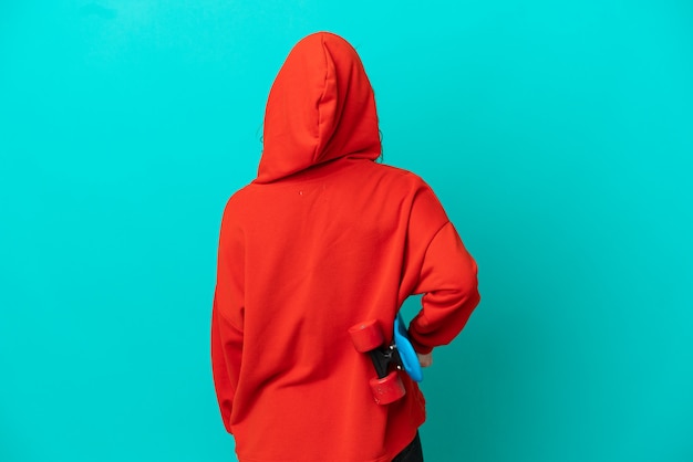 Рыжая девушка-подросток изолирована на синем фоне с коньком в заднем положении