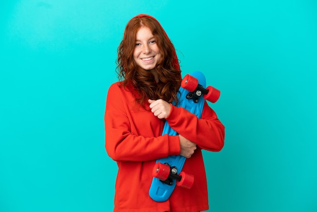 Teenager redhead girl isolated  on blue background with a skate with happy expression