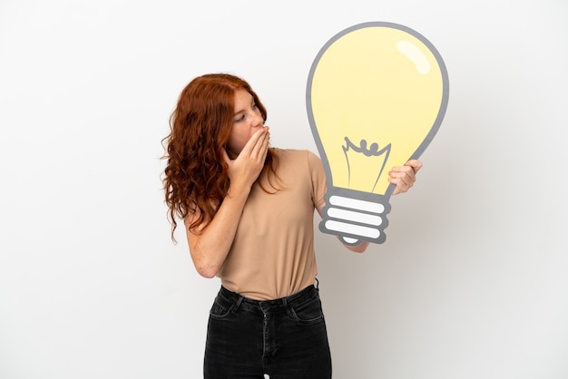 Teenager redhead girl isolated on white background holding a bulb icon with surprised expression