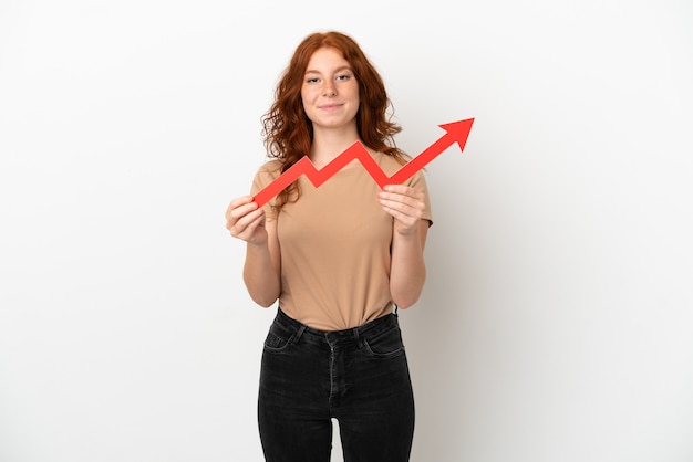 Teenager redhead girl isolated on white background holding a catching a rising arrow with happy expression