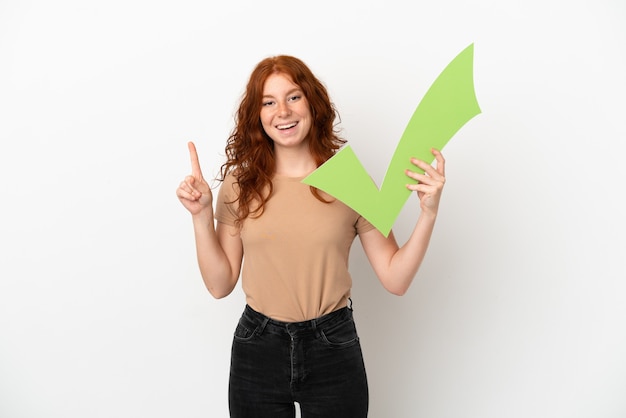 Photo teenager redhead girl isolated on white background holding a check icon and pointing up