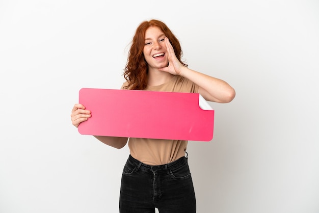 Teenager redhead girl isolated on white background holding an empty placard and shouting