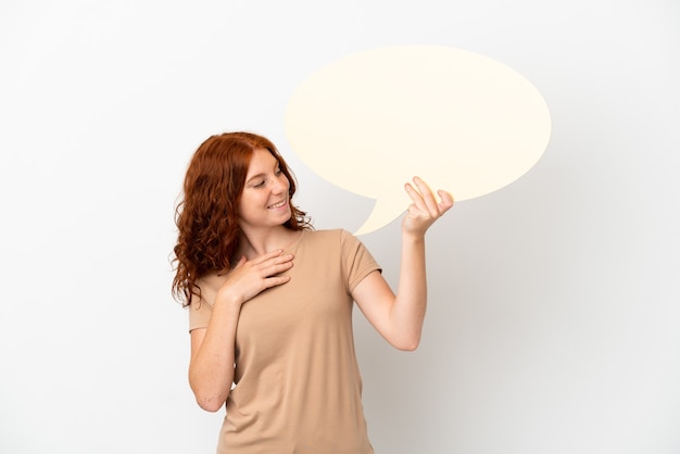 Teenager redhead girl isolated on white background holding an empty speech bubble and pointing it