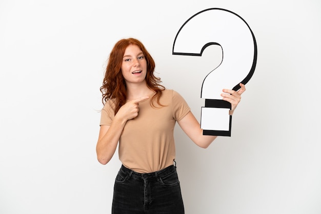 Teenager redhead girl isolated on white background holding a question mark icon with surprised expression