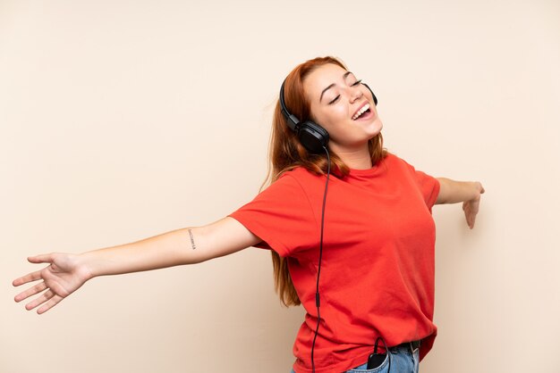 Teenager redhead girl listening music over isolated wall