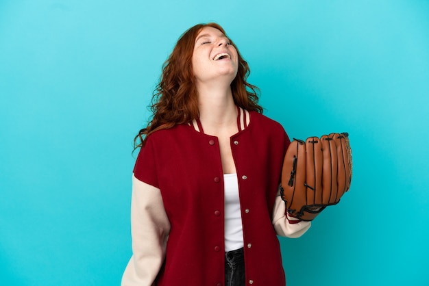 Ragazza rossa dell'adolescente con il guanto da baseball isolata su fondo blu che ride