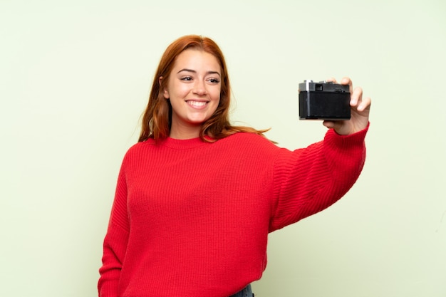 Teenager redhead girl with sweater over isolated green  making a selfie