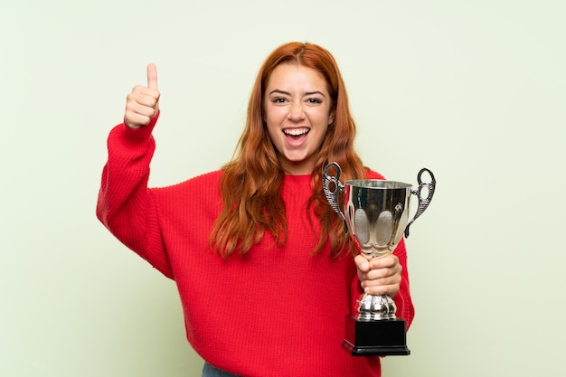 Фото Рыжая девушка подросток с свитер на зеленом фоне держит трофей