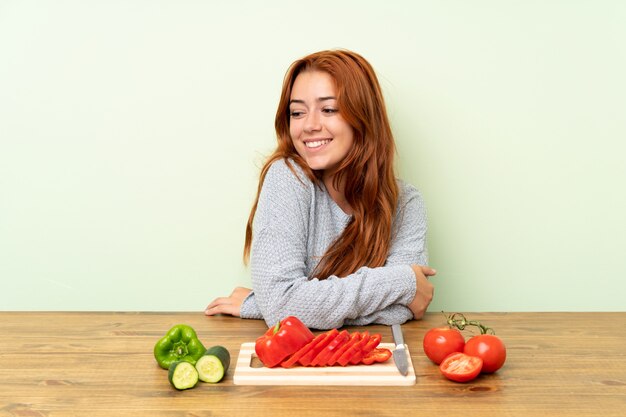 Teenager redhead girl with vegetables in a table laughing