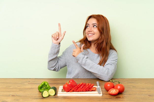 人差し指で素晴らしいテーブルを指しているテーブルで野菜とティーンエイジャーの赤毛の女の子