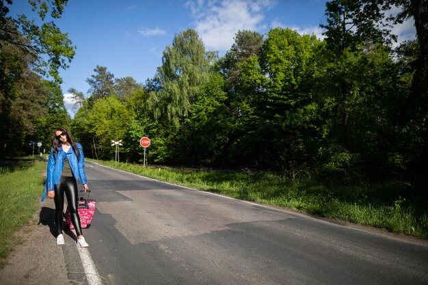 The teenager returns on foot along the asphalt road among lush greenery wonderful trees and shrubs