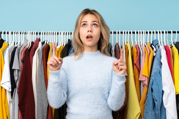 Teenager Russian girl buying some clothes on blue wall surprised and pointing up