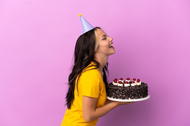 Teenager Russian girl holding birthday cake isolated on purple background laughing in lateral position