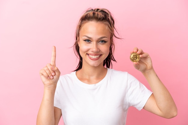 Teenager Russian girl holding a Bitcoin isolated on pink background pointing up a great idea