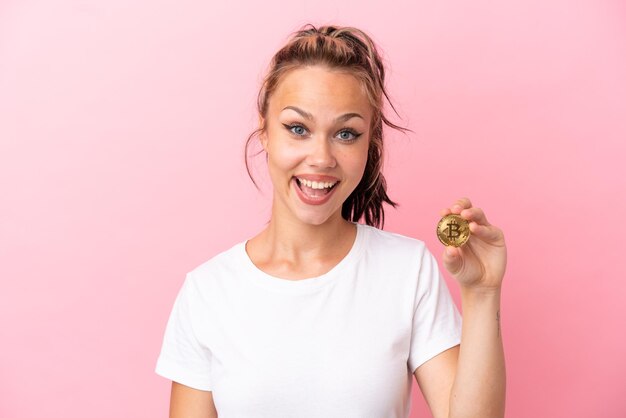 Teenager Russian girl holding a Bitcoin isolated on pink background with surprise facial expression