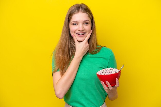 노란색 배경에 격리된 시리얼 그릇을 들고 행복하고 웃는 10대 러시아 소녀