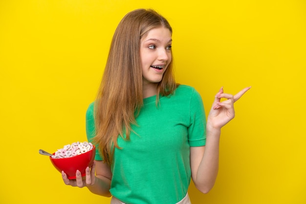 Teenager Russian girl holding bowl of cereals isolated on yellow background intending to realizes the solution while lifting a finger up